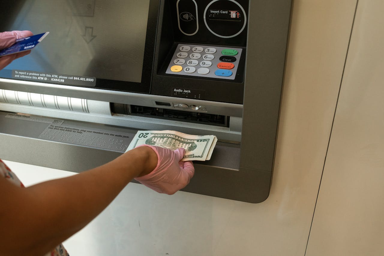 who-we-are A person wearing gloves withdrawing cash from an ATM machine showcasing money handling and hygiene.